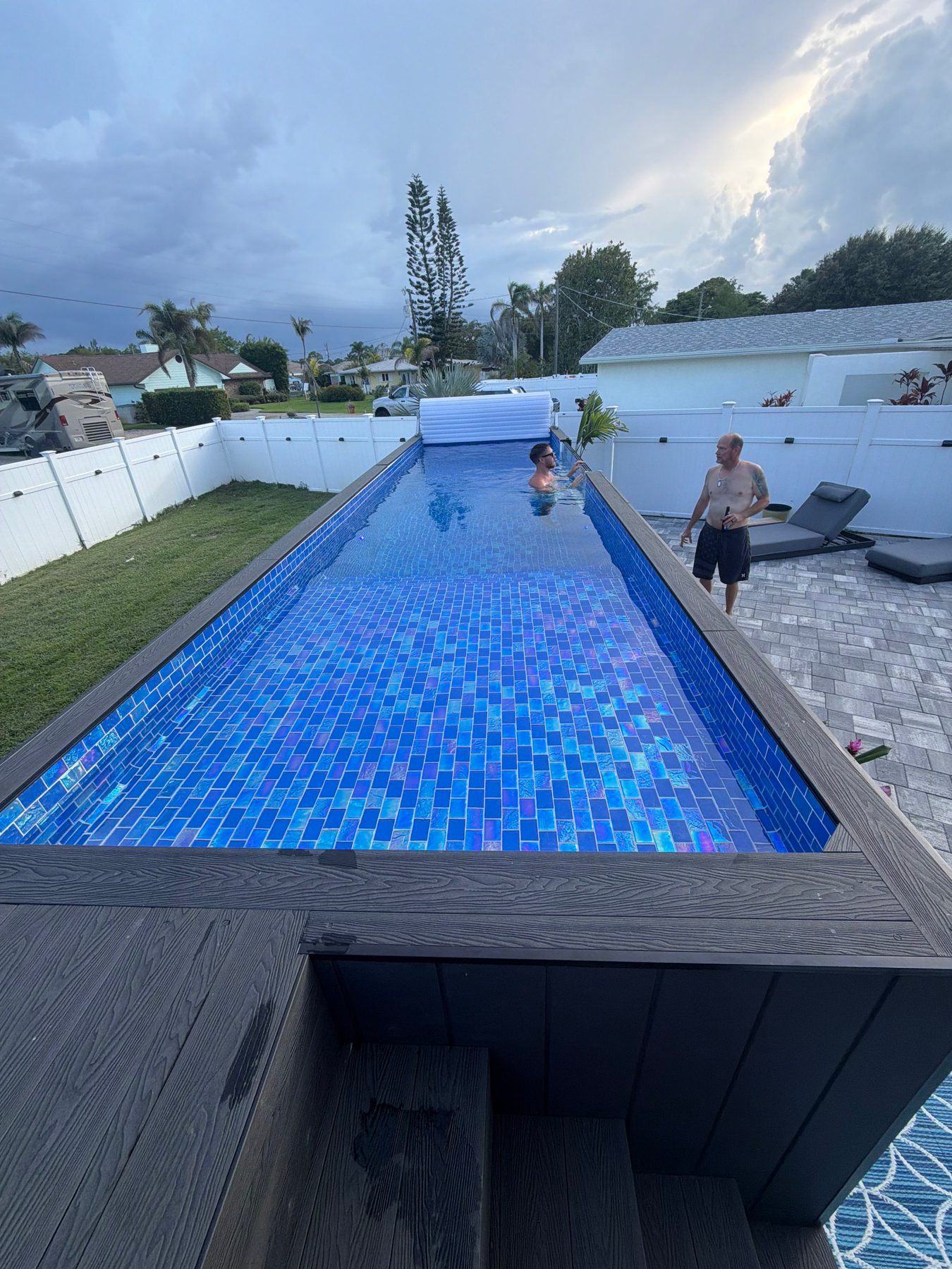 A mosaic plunge pool in a Florida backyard, cover rolled at the far end, two people beside the water.