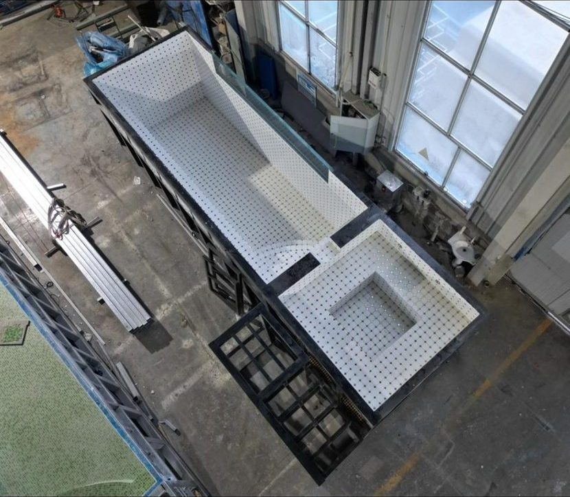 An empty pool-and-spa shell from above on the factory floor, white perforated panels inside.