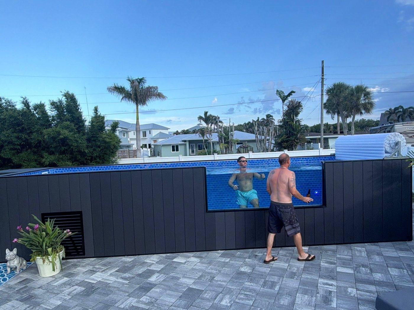 Two people at a dark plunge pool with an acrylic window, on a paver patio.